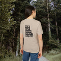 Frau von hinten im sandbeigen T-Shirt mit Katzen-Spruchprint zwischen Bäumen