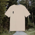 Sandbeiges Shirt mit feiner Tanne auf der Brust vor grünem Waldweg